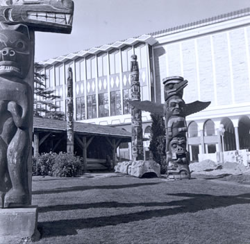 View of Totem Poles in Thunderbird Park with the Museum in the Background. 