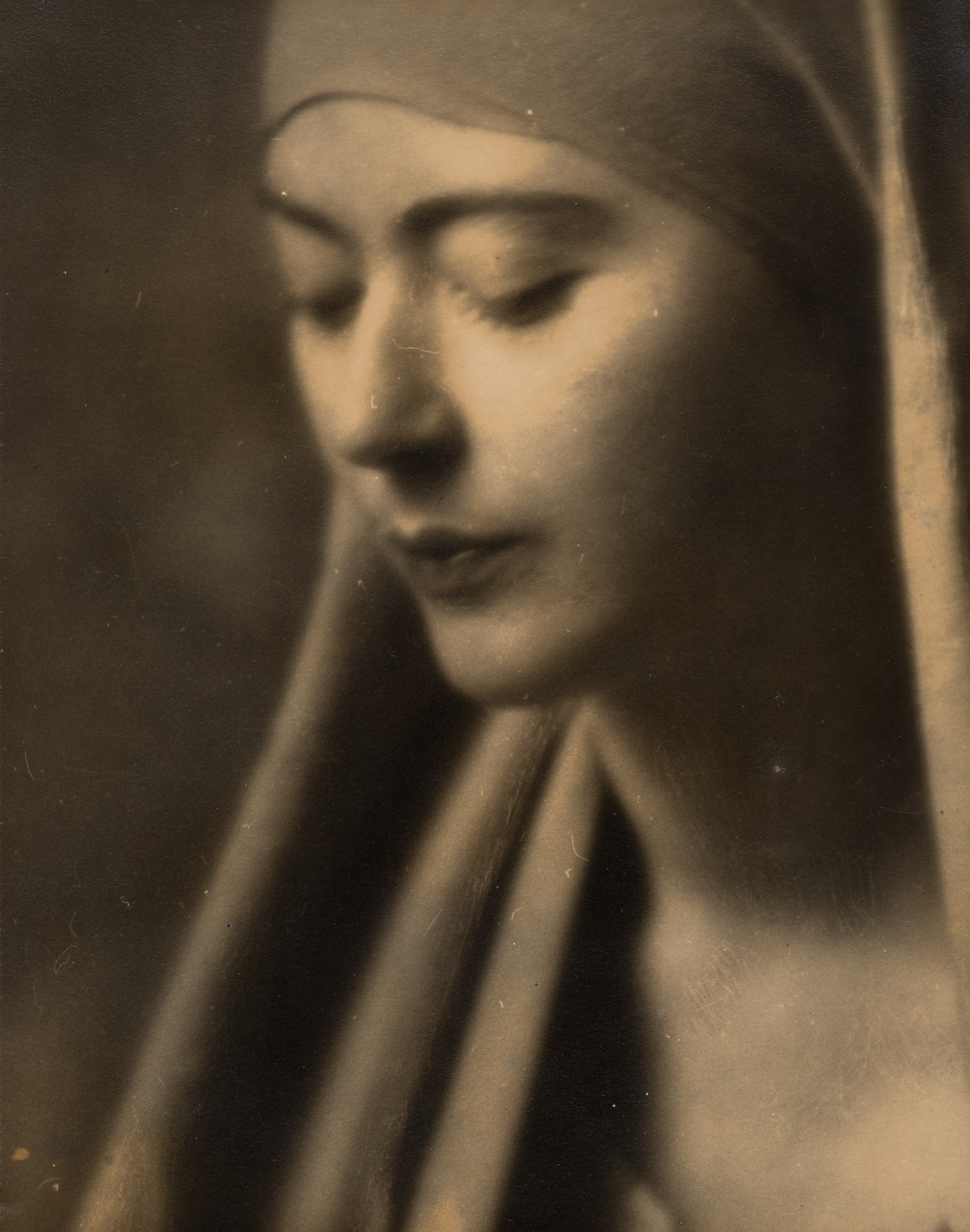 a black and white photographic portrait of a woman, showing her face and neck and wearing a head covering