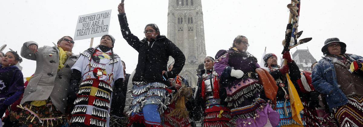 Indigenous women holding protest signs in front of the Canadian Parliament buildings in winter