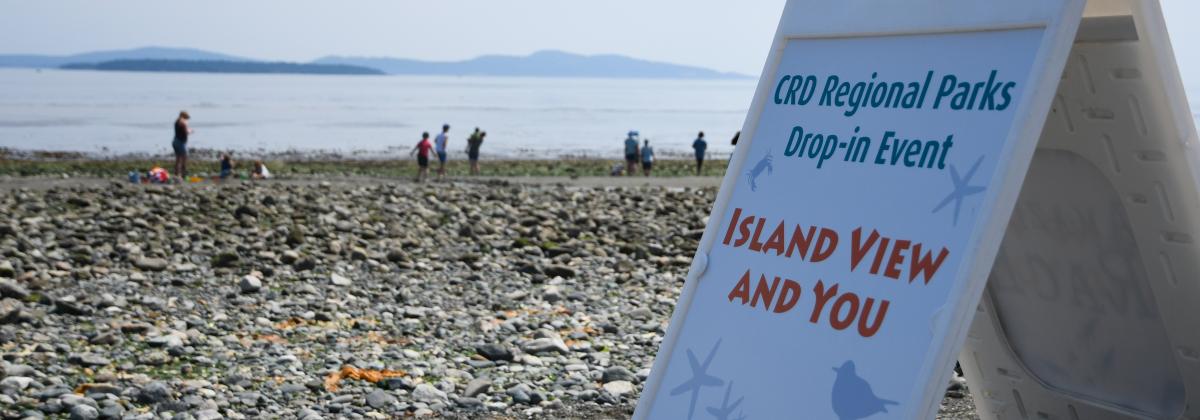 sandwich board sign in foreground, beach and ocean with islands in the distance. 