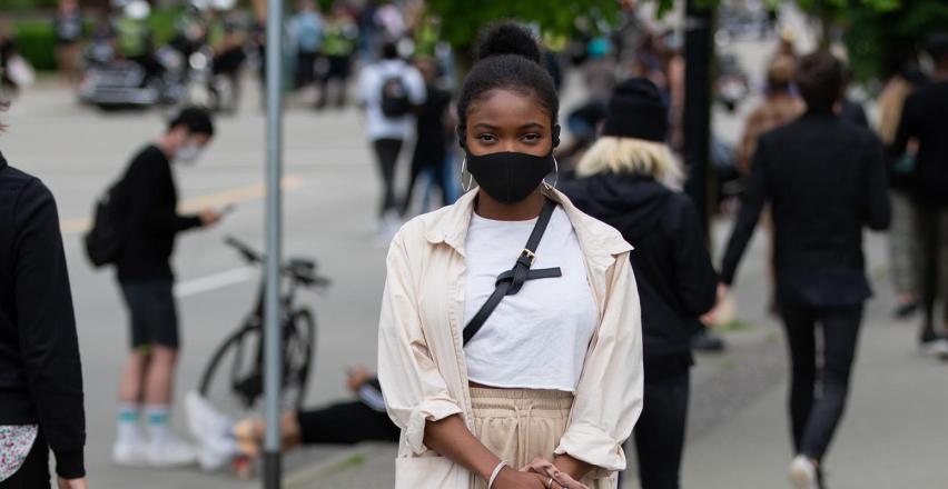 A woman wearing a black facemask standing on a busy sidewalk.