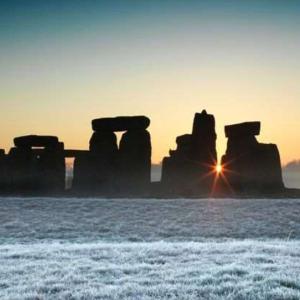 a landscape image of the Stonehenge monument during sunset, with snow on the ground